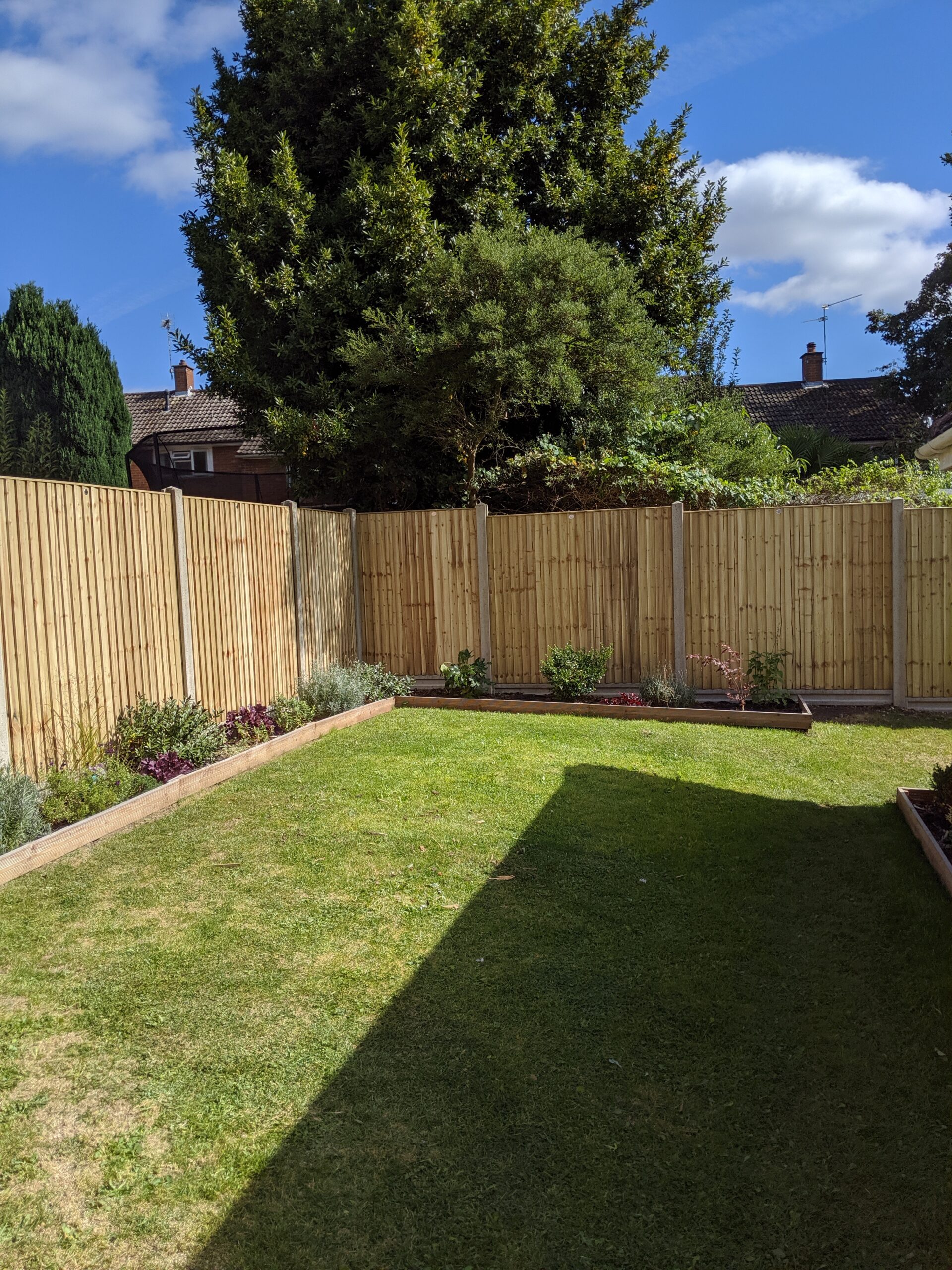 A garden with green closeboard panels concrete gravelboards and posts flower beds and grass
