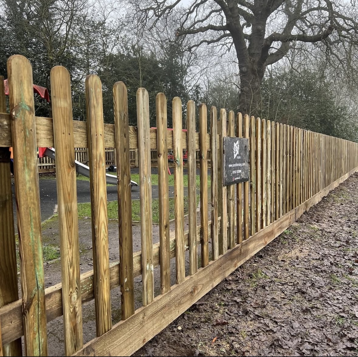 Round top picket fencing with timber posts and gravelboards S & B fencing sign attached